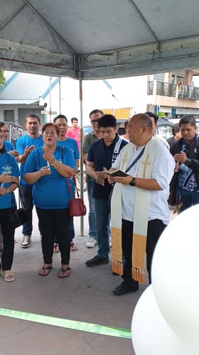 Grupo ng mga tao habang nagdarasal at may nagbabasbas sa ilalim ng canopy sa inagurasyon ng HOA Office