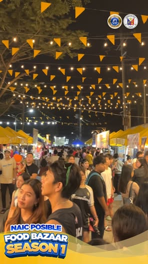 Mga tao sa Naic Posible Food Bazaar Season 1 sa gabi, may ilaw at bandila at mga food stall.