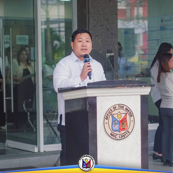 Lalaking nagsasalita sa mikropono sa podium ng Office of the Mayor, Naic, sa flag raising ceremony
