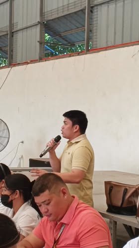 Lalaki na nagsasalita sa mikropono sa harap ng mga nakaupong dumalo sa loob ng hall sa Sabang, Naic
