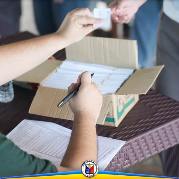 Pamamahagi ng educational assistance sa mesa, may kahon ng sobre at taong nagsusulat sa listahan