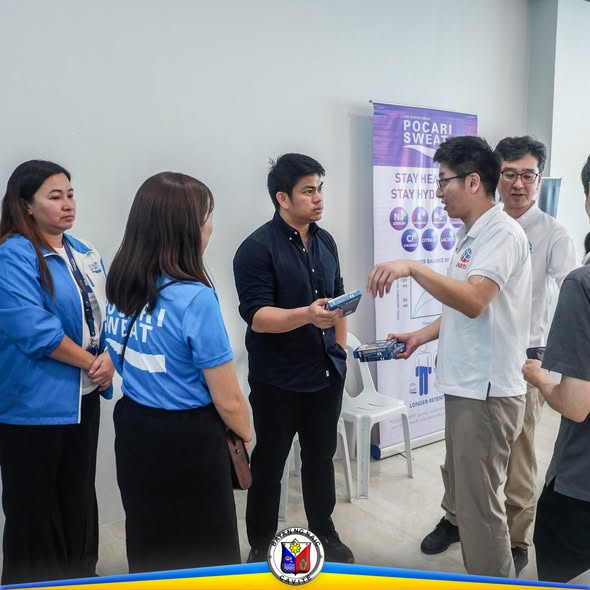 Mga tao na nag-uusap at may hawak na produkto sa loob ng event na may Pocari Sweat banner sa Triple 8, Naic