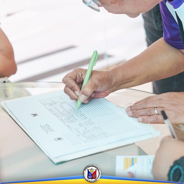 Taong nagsusulat sa form na may berdeng ballpen sa mesa habang isinasagawa ang Local Council of Women assembly
