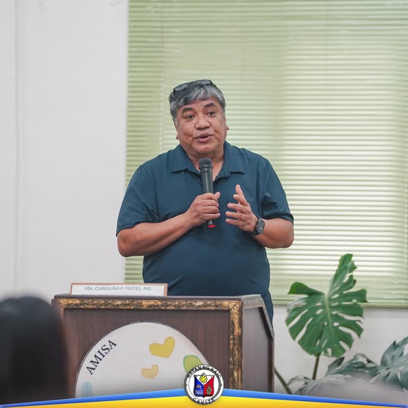 Lalaking nagsasalita sa mikropono sa podium ng Local Health Board Meeting sa Amisa Medical Mission Hospital, Naic