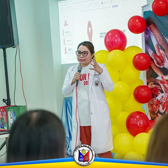 Babaeng naka-puting coat na nagsasalita sa mikropono sa harap ng screen at mga lobo sa isang pagtitipon
