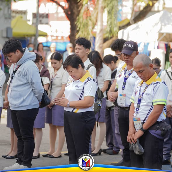 Mga kawani at mag-aaral na nakayuko habang nasa flag raising ceremony sa labas ng gusali sa Naic