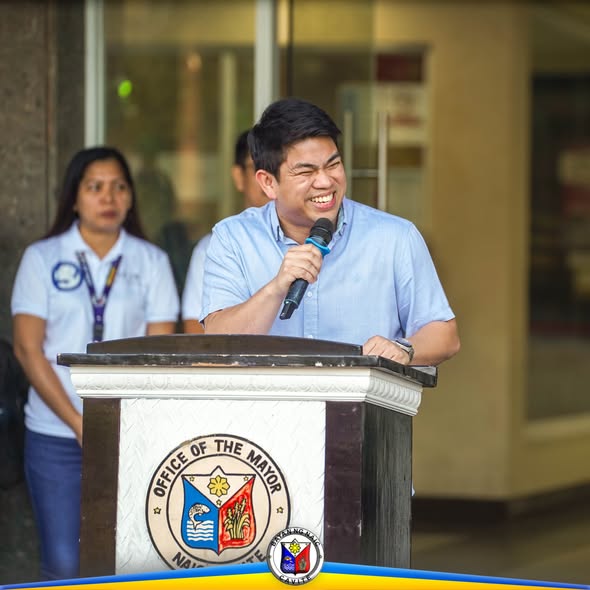 Mayor na nagsasalita sa mikropono sa podium ng Office of the Mayor sa harap ng Naic Municipal Hall