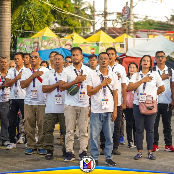 Mga kawani ng pamahalaang bayan na nakatayo at nakahawak sa dibdib habang nag-aawit ng pambansang awit sa flag raising
