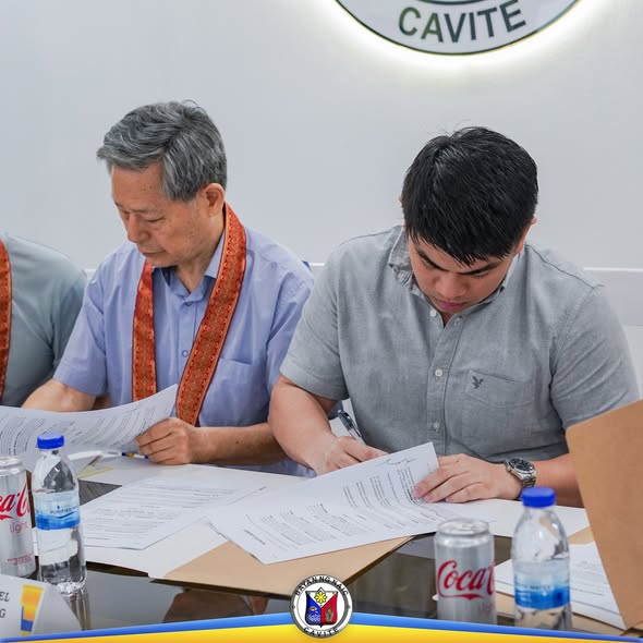 Dalawang lalaki habang pumipirma ng dokumento sa mesa sa Naic Municipal Hall