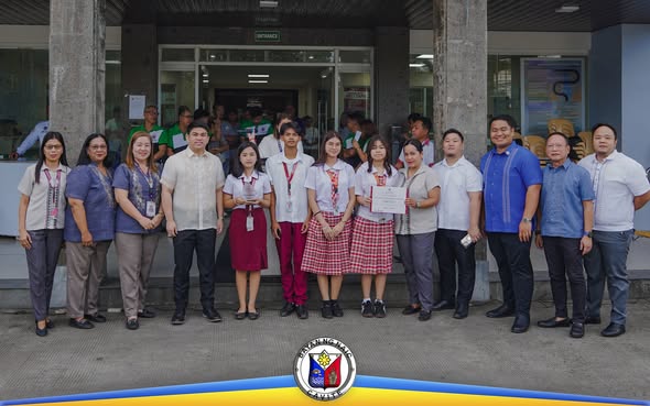 Grupo ng mga kawani at mag-aaral na nakatayo sa harap ng gusali habang may hawak na sertipiko