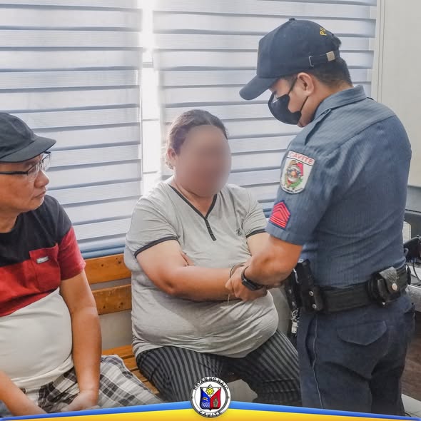 Pulis na nagposas sa babaeng nakaupo sa bench habang may kasamang lalaki sa loob ng opisina