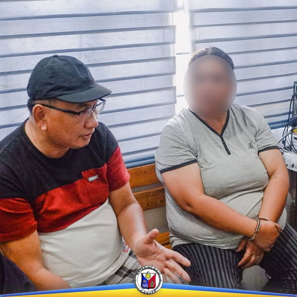 Litrato: lalaking nagsasalita habang may kasamang taong nakaposas ang kamay sa loob ng opisina
