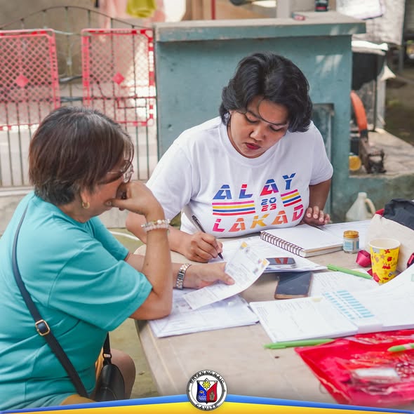 Mga kababaihan na nagsasagawa ng pagpaparehistro ng mga magsasaka sa isang mesa sa labas