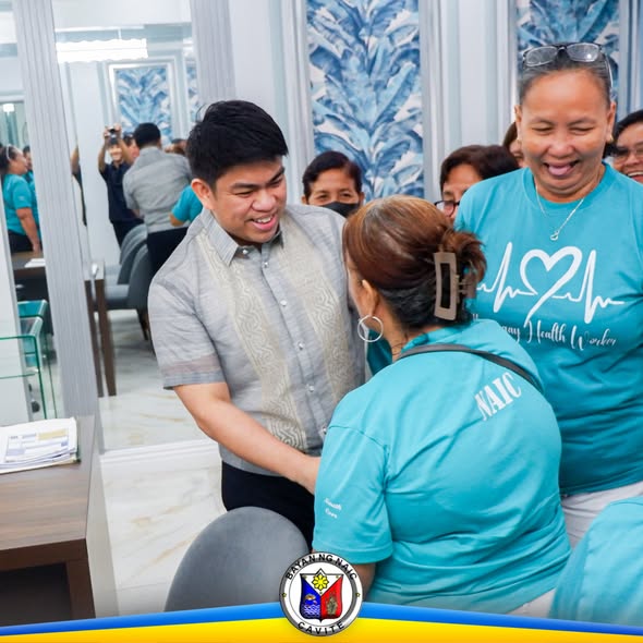 Mga BHW na naka-teal na t-shirt habang binabati ng isang opisyal sa loob ng Naic Municipal Hall