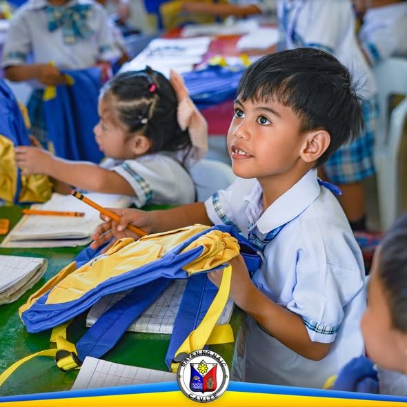 Mga mag-aaral na may hawak na school bag habang nakikinig sa loob ng silid-aralan sa Naic