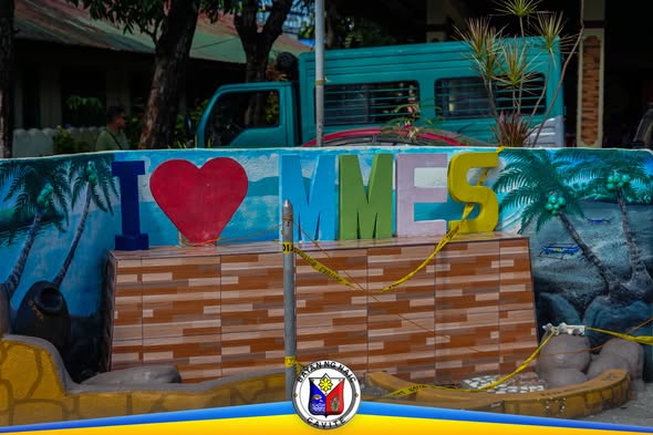 Makulay na signage na "I Love MMES" na may dilaw na caution tape sa Munting Mapino