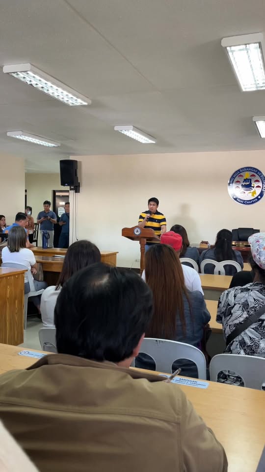 Pulong sa silid-pulungan kung saan nagsasalita ang isang lalaki sa podium habang nakikinig ang mga dumalo
