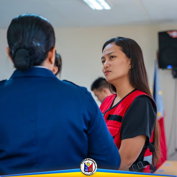 Pulis na kausap ang babaeng nakasuot ng pulang vest sa loob ng silid