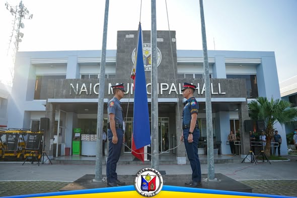 Flag raising ceremony sa harap ng Naic Municipal Hall, may dalawang naka-unipormeng tauhan na nakatayo sa tabi ng watawat