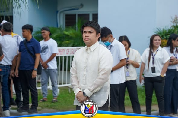 Mga kawani at mag-aaral habang nakatayo sa flag raising ceremony ng Naic, may lalaking naka-barong sa harap