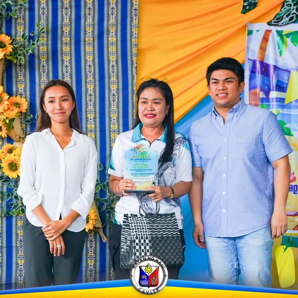 Tatlong tao na may hawak na certificate of appreciation sa harap ng backdrop na may sunflower