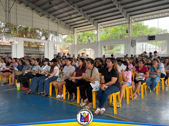 Mga kababaihang nakaupo sa covered court habang nakikinig sa briefing ng libreng HPV vaccination sa Naic