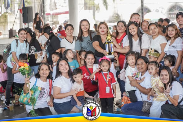 Grupo ng mga nanay at mga bata na nagpapose kasama ang tropeo sa Nutrition Month sa Naic Town Plaza