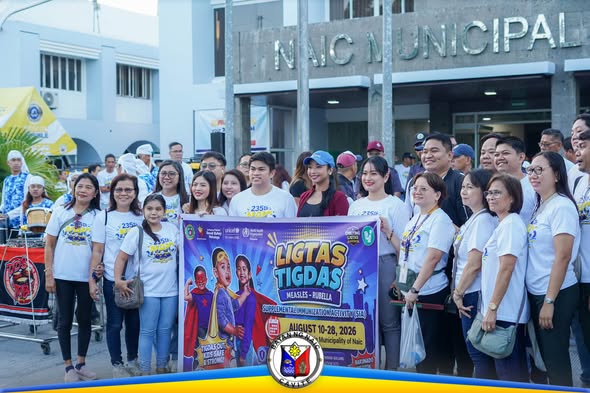 Grupo ng mga kawani at opisyal na may hawak na banner ng Ligtas Tigdas campaign sa harap ng Naic Municipal