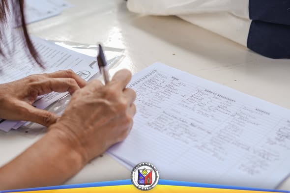 Kamay na nagsusulat sa listahan ng mga nagpatala sa Birth Registration Assistance Project sa Bancaan