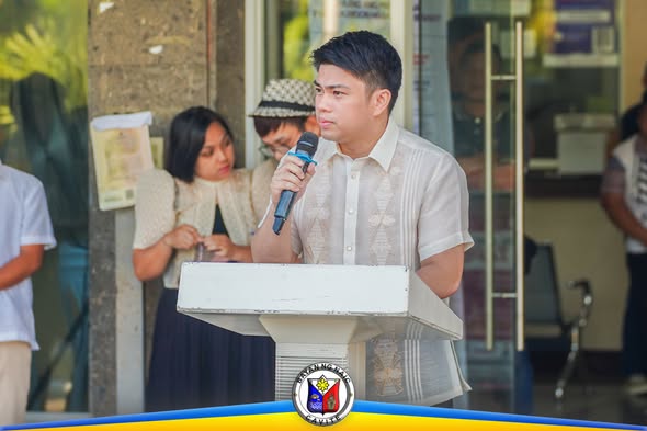 Lalaking nagsasalita sa mikropono sa podium habang nasa flag raising ceremony sa Naic Municipal Hall
