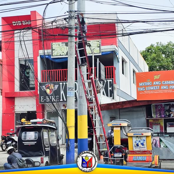 Manggagawa na umaakyat sa poste ng kuryente para sa cable clearing sa harap ng Naic Municipal Hall, Ibayo Silangan