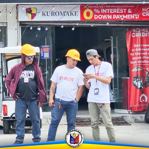 Mga tauhan ng PLDT na may suot na hard hat habang tumitingin sa cellphone sa kalsada malapit sa Naic Municipal Hall