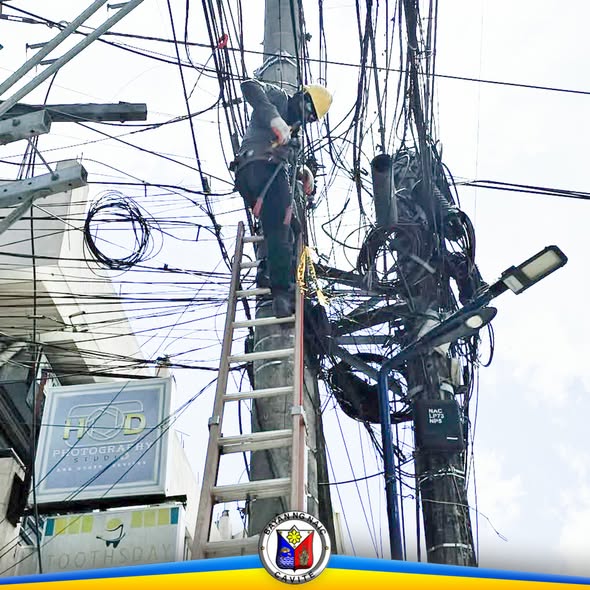 Manggagawa na umaakyat sa poste at nag-aayos ng magulong kable sa Naic Municipal Hall frontage, Brgy. Ibayo Silangan