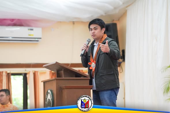 Lalaki na nagsasalita sa mikropono sa entablado habang nagtuturo sa talakayan ng Naic
