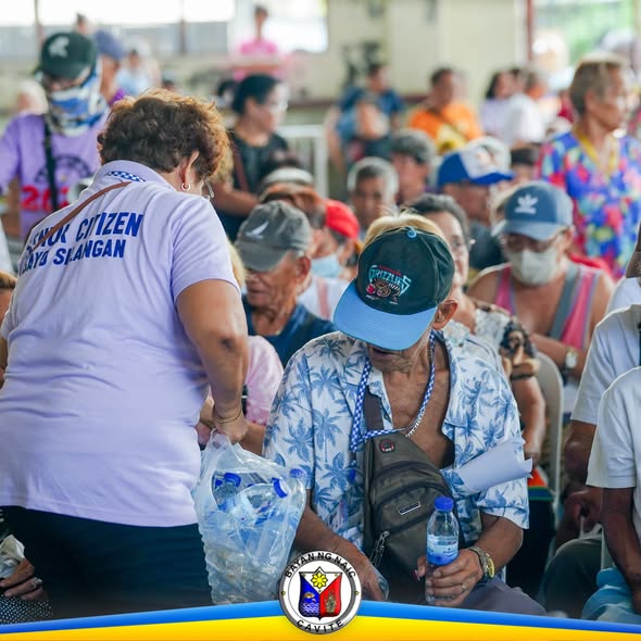 Mga senior citizen na nakaupo habang may kawaning namimigay ng tubig sa National Social Pension Payout sa Naic