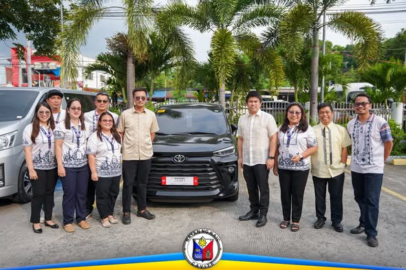 Mga kawani at opisyal ng bayan na nagpose sa harap ng bagong sasakyan sa labas ng tanggapan