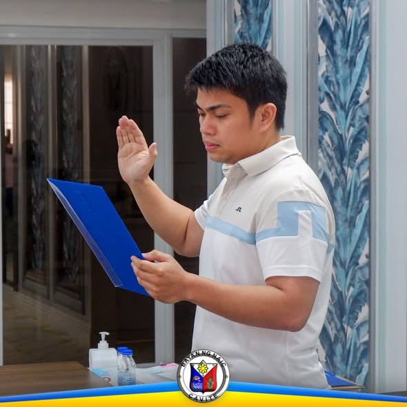 Lalaking nanunumpa habang nakataas ang kanang kamay at hawak ang asul na folder sa loob ng opisina
