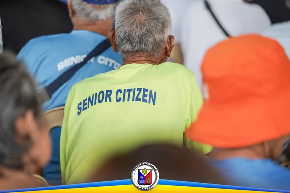 Mga senior citizen na nakaupo at nakikinig sa National Social Pension Distribution sa Naic Town Plaza