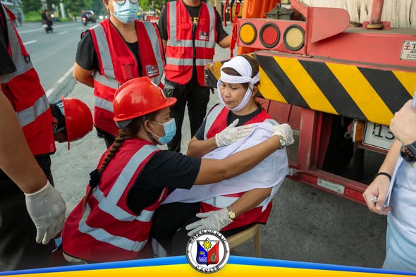 Mga responder na tinatapalan ng benda ang braso ng isang kalahok sa Naic Emergency Response Challenge sa tabi ng trak