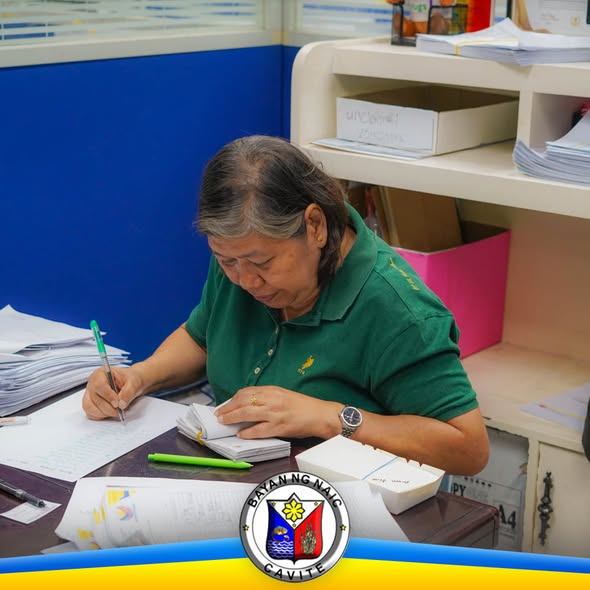 Babaeng kawani ng OSCA na nagsusulat ng talaan sa opisina habang may hawak na mga papel