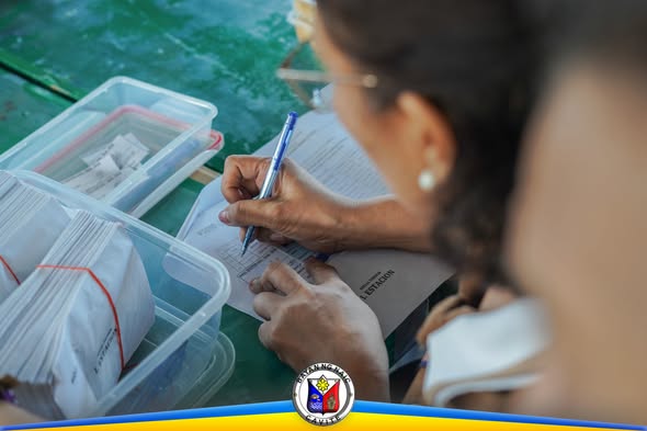 Taong nagsusulat sa papel habang nakaupo sa mesa na may mga lalagyan ng dokumento sa pamamahagi ng pensyon