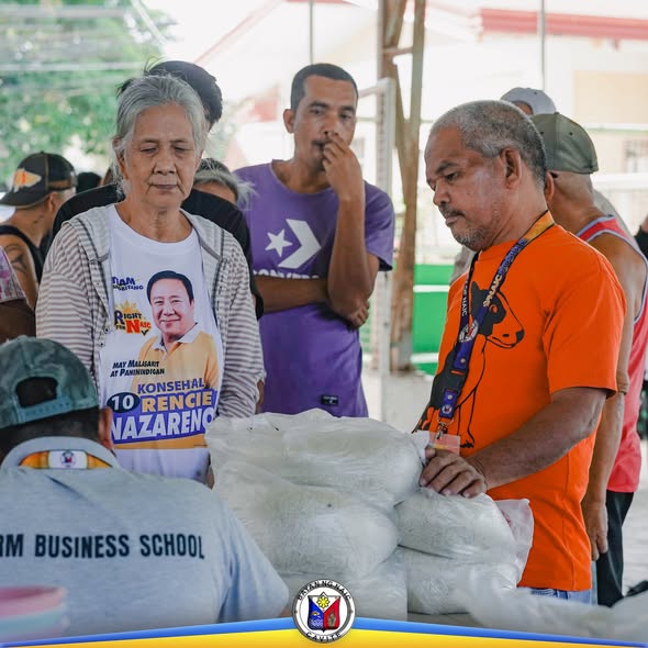 Mga tao sa KADIWA Rice Selling habang may nakasalansan na sako ng bigas sa covered court ng Labac