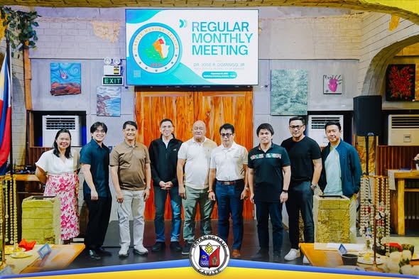 Grupo ng mga kalalakihan at babae na nagpose sa harap ng screen na may nakasulat na Regular Monthly Meeting