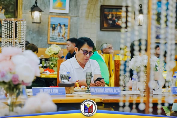 Lalaki na nakaupo sa hapag-kainan habang tumitingin sa cellphone sa pulong ng Cavite Mayors' League