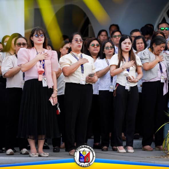 Mga kawani ng Naic habang nakatayo at nakahawak sa dibdib sa flagraising ceremony sa Municipal Hall