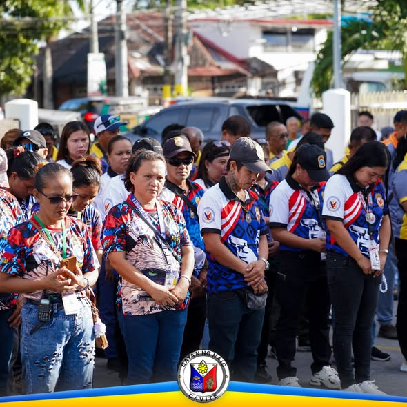 Mga kawani ng lokal na pamahalaan na nakayuko at nakahanay habang nagaganap ang flag raising ceremony sa Naic