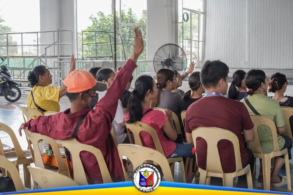 Mga taong nakaupo sa covered court habang nagtataas ng kamay sa Influenza Vaccination program sa Naic