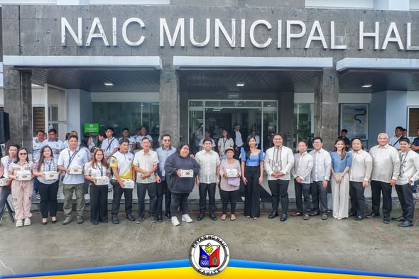 Grupo ng mga tao na may hawak na puting kahon sa harap ng Naic Municipal Hall