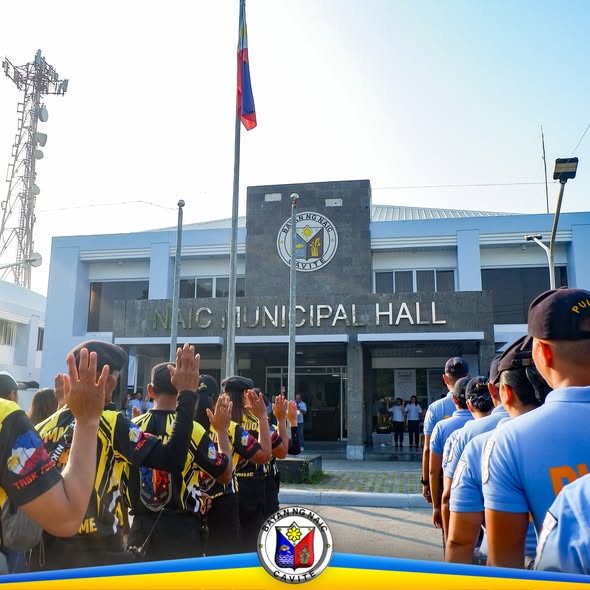 Flag raising ceremony sa harap ng Naic Municipal Hall, may mga nakahanay na kalahok at watawat.