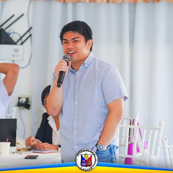 Lalaking nagsasalita gamit ang mikropono sa Revenue Code Seminar sa Naic, may mga puting upuan at kurtina sa likod